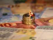 Brief- en muntgeld met bovenop een stapeltje munten twee miniatuurfiguren